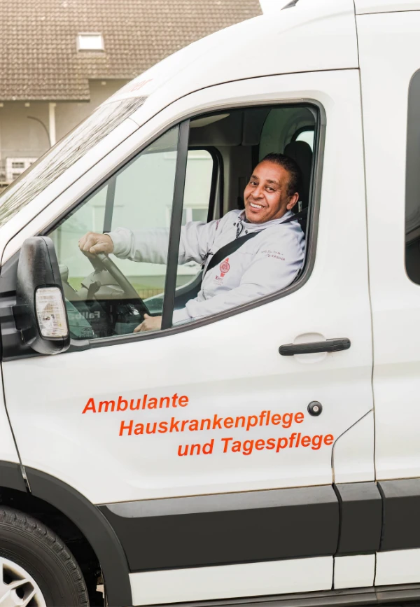 Mitarbeiter sitzt am Steuer und lächelt aus dem offenen Fenster in die Kamera