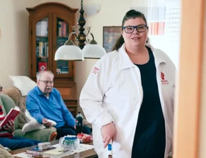 Eine freundliche Pflegekraft vom Pflegedienst Kremer bei der hochwertigen ambulanten Pflege eines älteren Ehepaares in deren privatem Wohnzimmer.