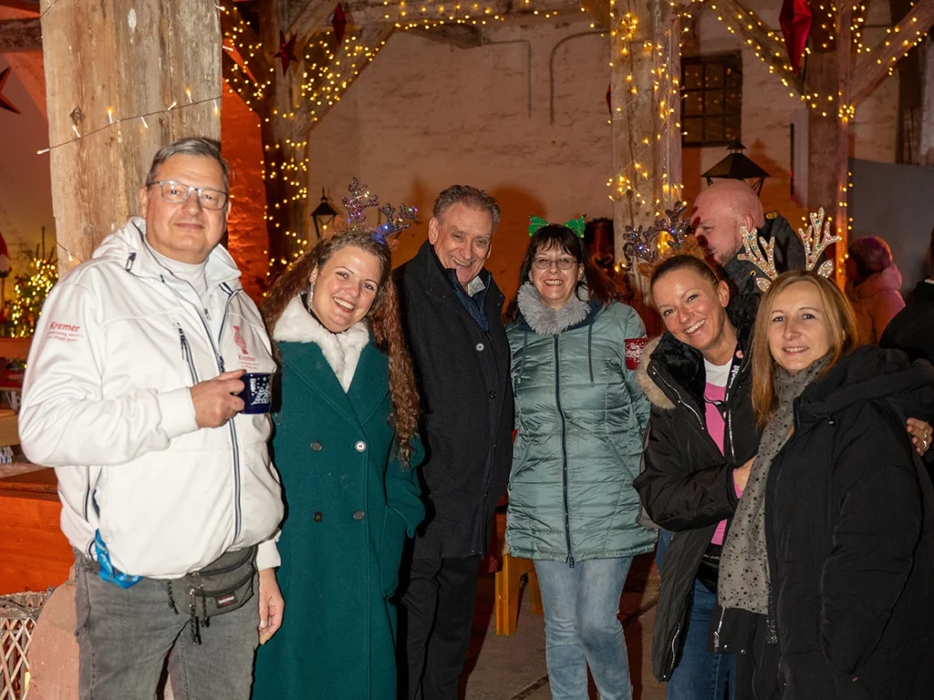 Mehrere Personen auf dem Weihnachtsmarkt nebeneinander stehend lächeln in die Kamera