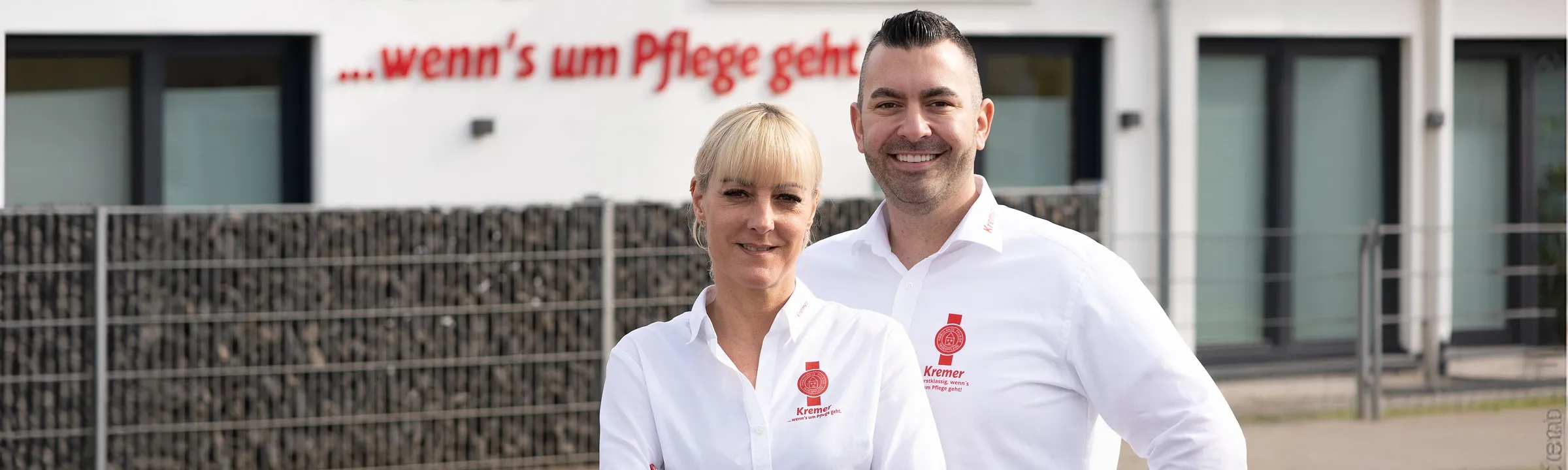 Zwei freundliche Mitarbeiter vom Pflegedienst Kremer vor dem Firmengebäude für ambulante Pflege im Main-Kinzig-Kreis bei der Pflegeberatung.