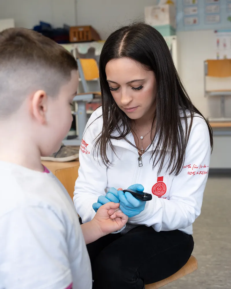 Eine Pflegekraft vom Pflegedienst Kremer führt bei einem Kind eine professionelle Blutzuckermessung im Rahmen der ambulanten Pflege im MKK durch.