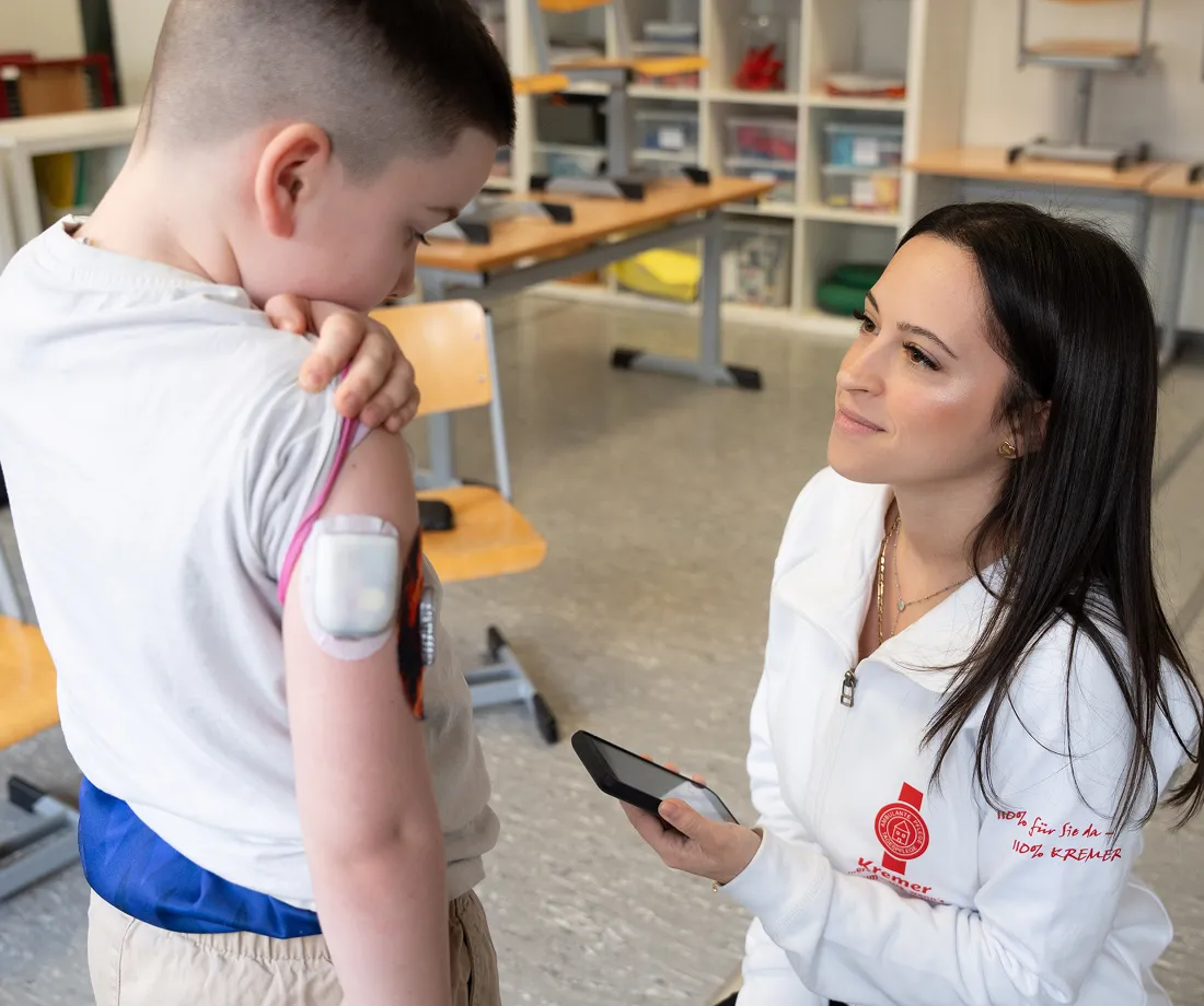 Eine Pflegekraft vom Pflegedienst Kremer betreut liebevoll ein Kind bei der Kinderintensivpflege und prüft dessen medizinischen Sensor am Arm.