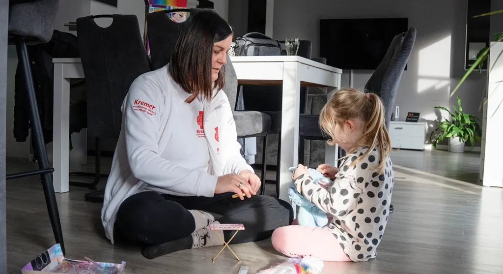 Eine Pflegekraft vom Pflegedienst Kremer spielt liebevoll mit einem Kind im Wohnzimmer, ein Beispiel für hochwertige Kinderintensivpflege zu Hause.