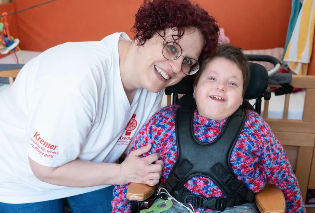 Eine freundliche Pflegekraft von Pflegedienst Kremer betreut liebevoll ein Kind im Rollstuhl im Rahmen der professionellen Kinderintensivpflege.