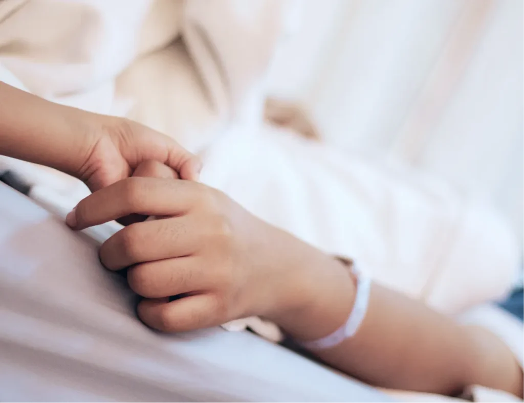 Eine Hand hält liebevoll die Hand eines Kindes im Bett als Symbol für die hochwertige Kinderintensivpflege durch den Pflegedienst Kremer.