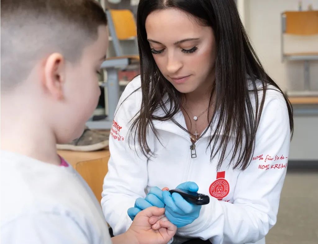 Eine Pflegekraft vom Pflegedienst Kremer führt bei einem Kind eine Blutzuckermessung durch, ein wichtiger Teil der ambulanten Pflege im MKK.