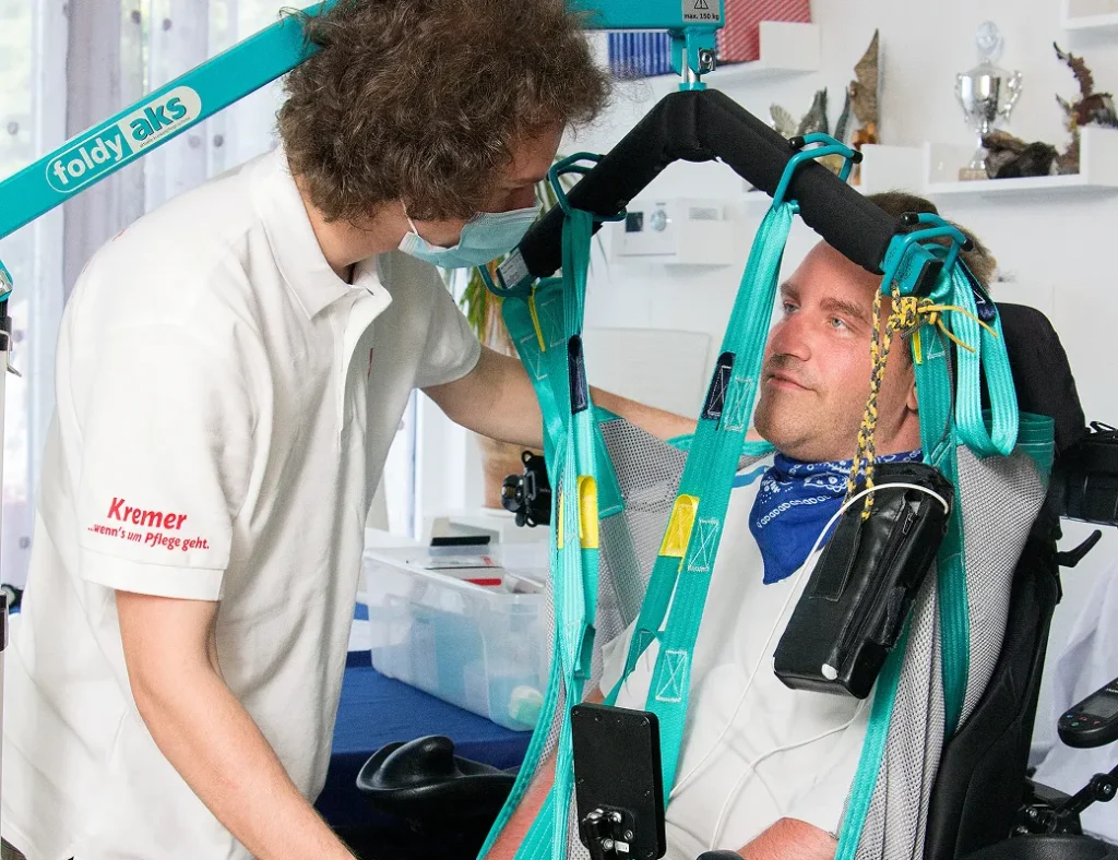 Eine Pflegekraft vom Pflegedienst Kremer unterstützt einen Klienten bei der Außerklinischen Intensivpflege mit einem Patientenlifter in häuslicher Umgebung.