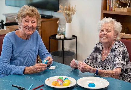 Zwei zufriedene Seniorinnen beim gemeinsamen Basteln und Bemalen von Eiern während der Tagespflege bei Pflegedienst Kremer für hochwertige Pflege.