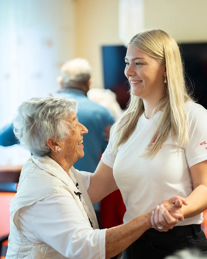 Eine freundliche Pflegekraft vom Pflegedienst Kremer unterstützt eine Seniorin bei der Tagespflege MKK mit einem herzlichen Lächeln und Zuwendung.