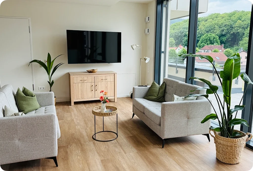Ein heller, modern eingerichteter Wohnbereich für die hochwertige Pflege durch Pflegedienst Kremer mit gemütlichen Sofas und bodentiefen Fenstern.