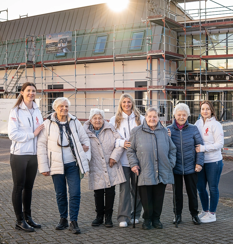 Mitarbeiterinnen von Kremer stehen zusammen mit Klientinnen vor dem neuen Tagespflege-Gebäude
