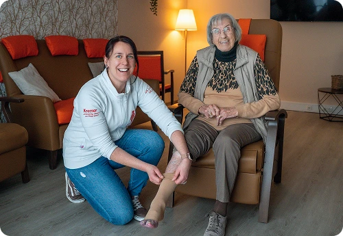 Eine freundliche Pflegekraft vom Pflegedienst Kremer unterstützt eine Seniorin bei der hochwertigen Pflege und dem Anlegen eines Kompressionsstrumpfes.