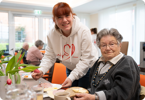 Eine freundliche Pflegekraft vom Pflegedienst Kremer unterstützt eine Seniorin bei der Tagespflege mit hochwertiger Pflege in einer hellen Umgebung.